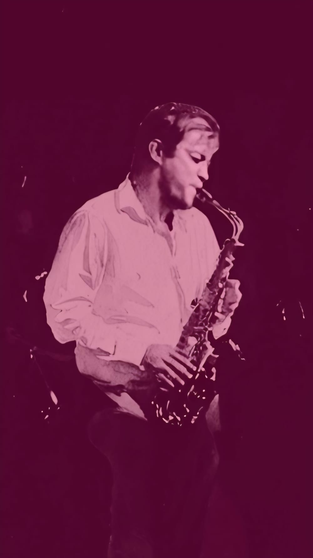 Jonah playing saxophone on a dark stage, in a magenta-toned photo.